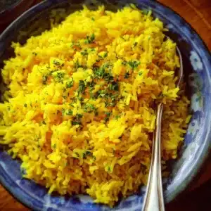 Bowl of vibrant turmeric rice garnished with herbs and spices